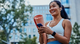 Smiling woman with yoga mat walking in park