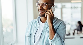 Man in light denim shirt with clear-framed glasses speaking on smartphone