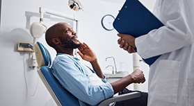 Man in denim shirt in dental chair looking at dentist in white coat