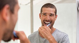Man smiling while brushing his teeth in bathroom