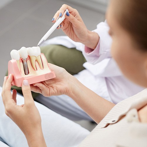 Dentist pointing to sample dental implant held by patient