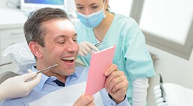 Man in dental chair smiling into mirror with dentist behind shoulder