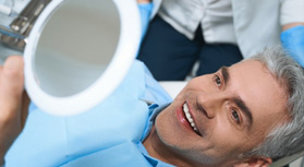 a patient smiling and checking his teeth with a mirror