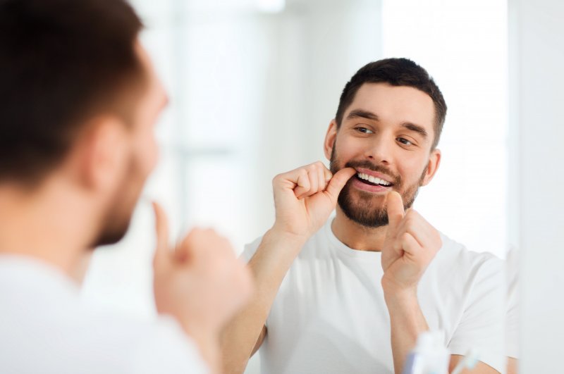 man flossing in bathroom mirror