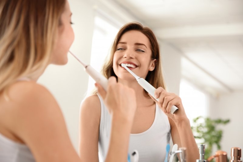 A woman smiling in the mirror as she uses her electric toothbrush