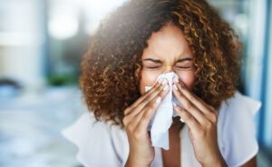 Woman with brown hair sneezing into a tissue