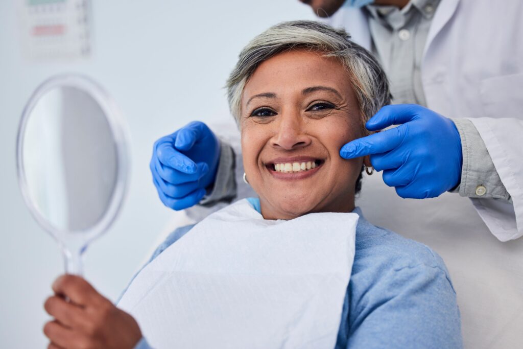 Woman with gray hair smiling as dentist touches her cheek
