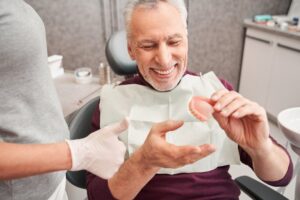 Man smiling while handing his dentures to his dentures