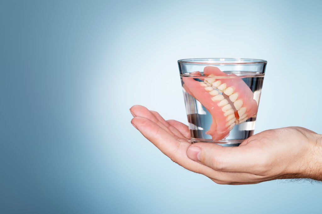 Dentures in a glass of clear fluid resting on the palm of a hand