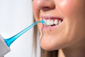 Closeup of woman using blue-tipped oral irrigator to clean gums